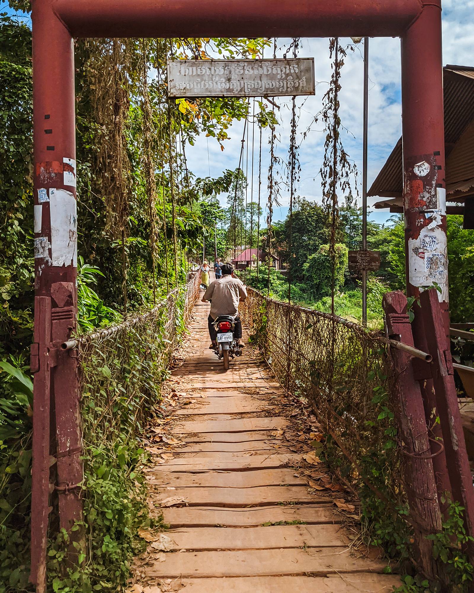 Man riding a motorbike on the Kampong Pil suspension bridge in Battambang, Cambodia