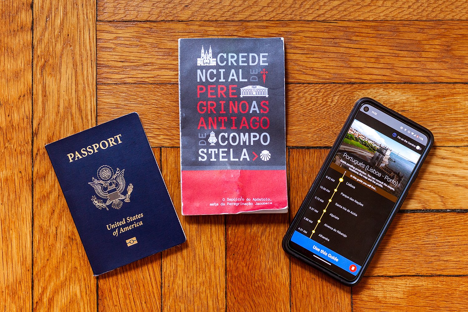 Passport, Camino de Santiago pilgrim credential, and Buen Camino app flatlay on a wood floor
