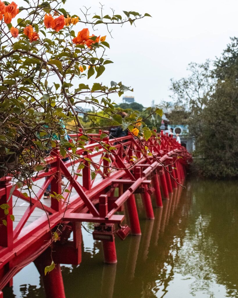 Orange flowers and red bridge leading to Ngoc Son Temple
