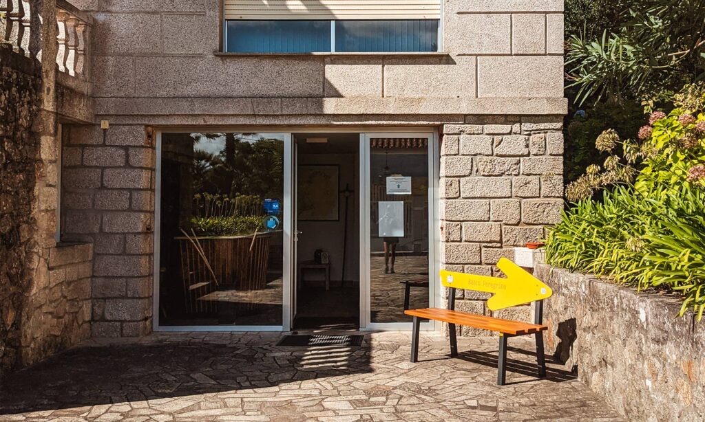 Entrance doors and a yellow arrow bench outside at Albergue Pallanes